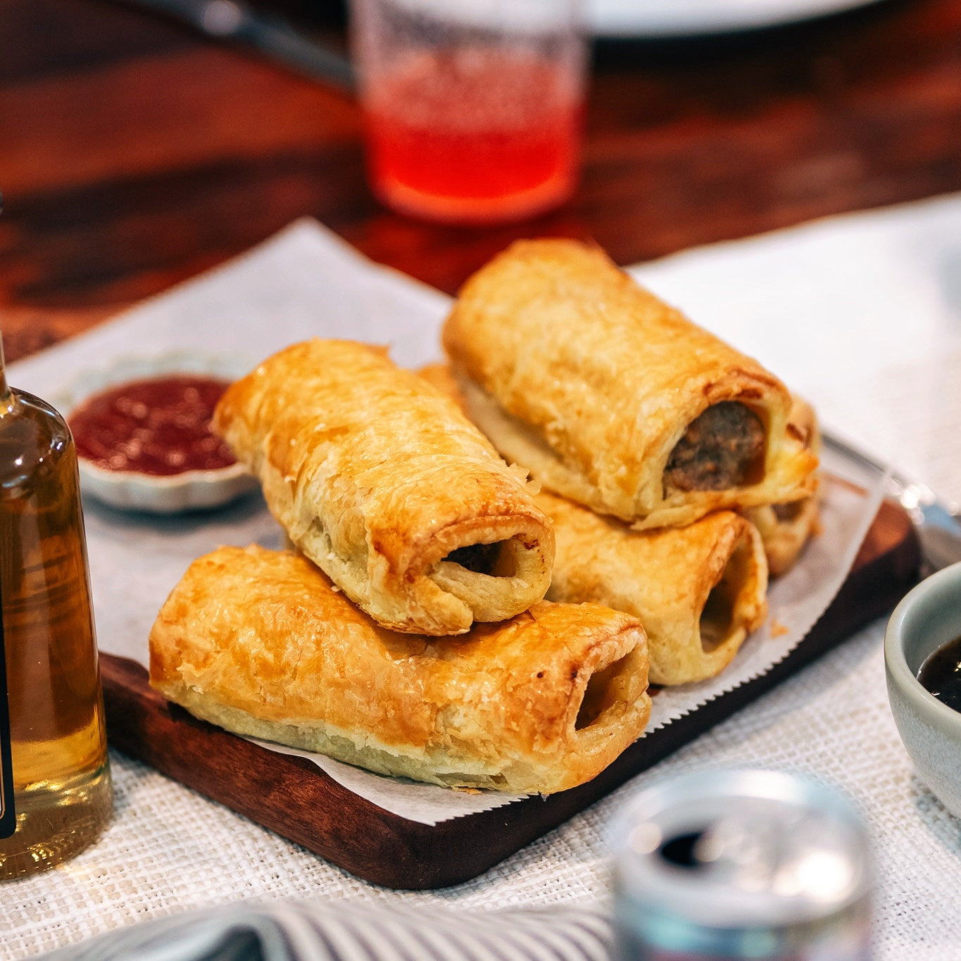 Pork sausage rolls 4 pack displayed on a wooden platter with dipping sauce, perfect for comfort food lovers.