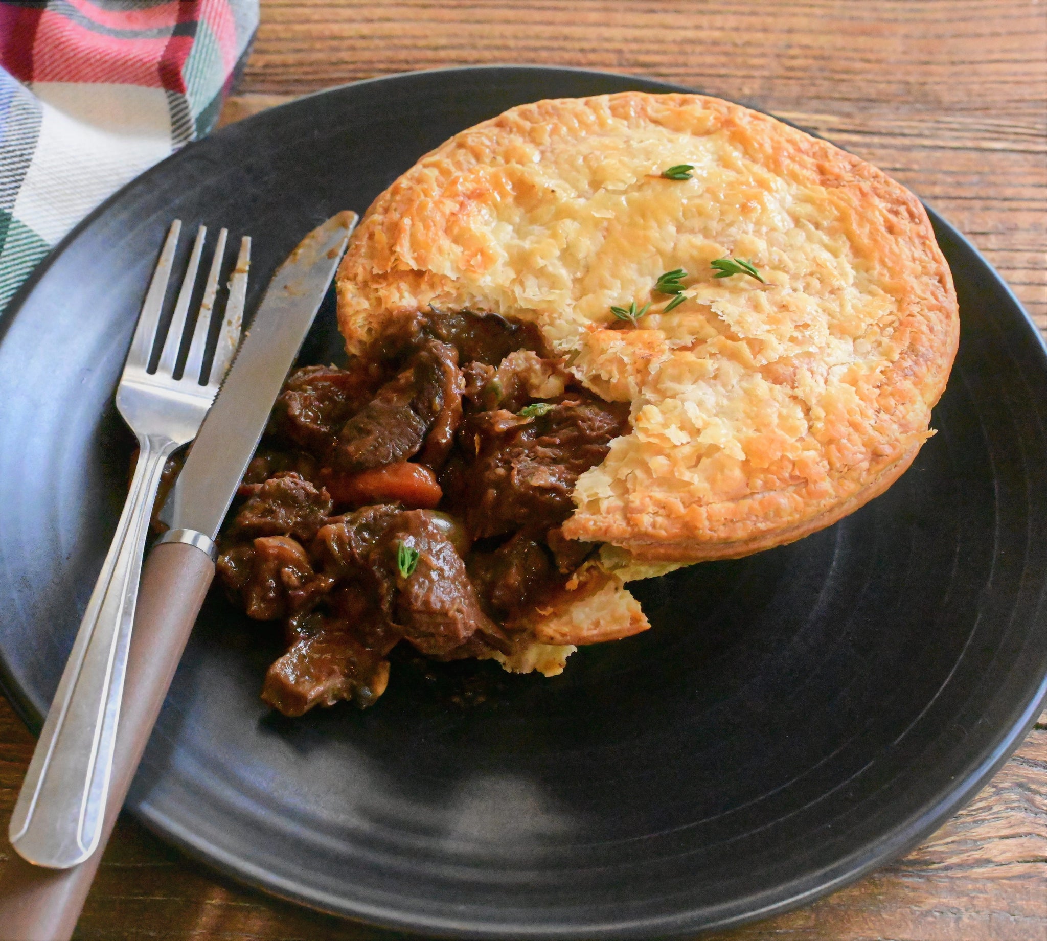 Delicious MOOLIN ROUGE beef bourguignon pie with tender steak and flaky pastry on a black plate.