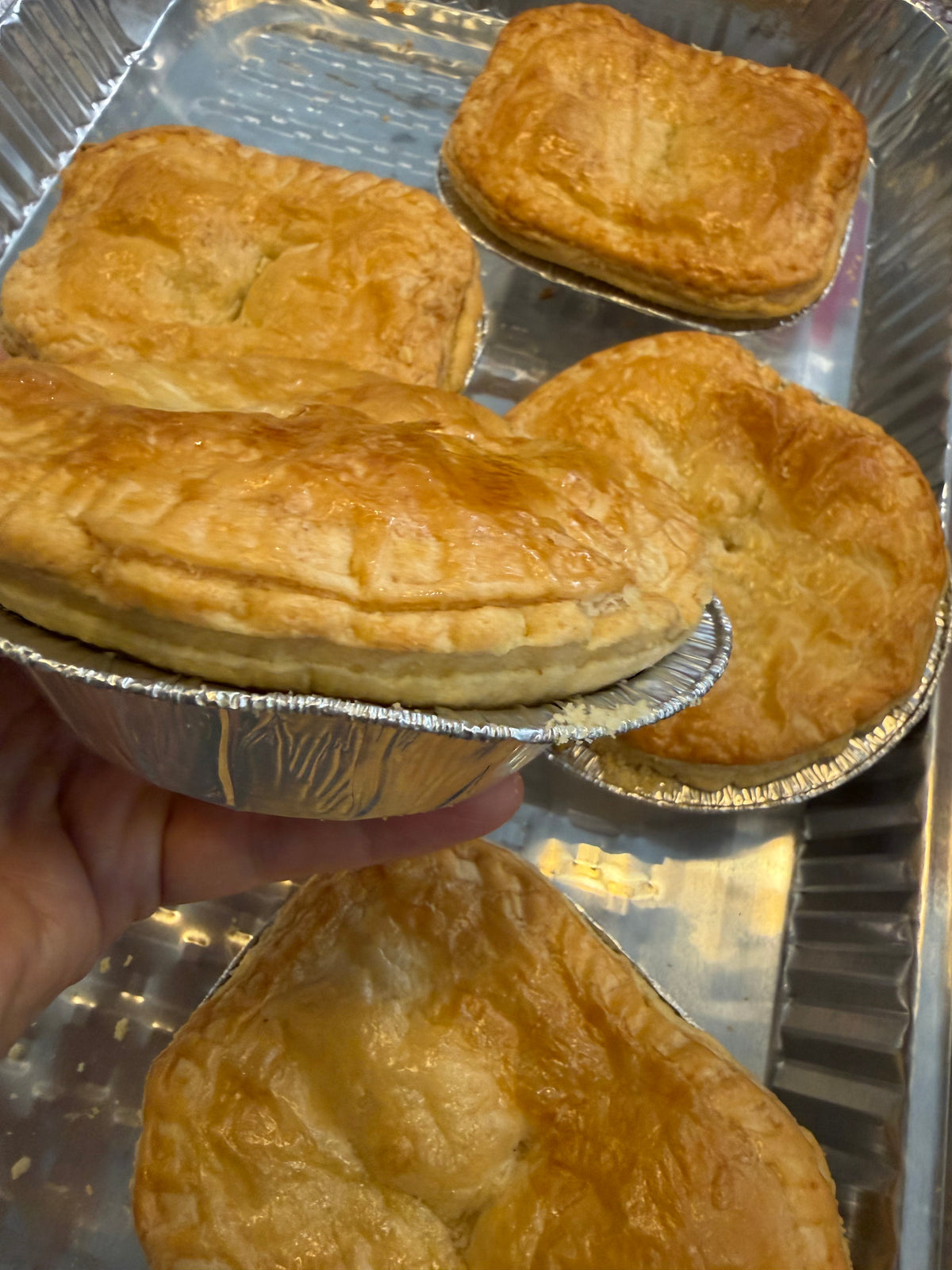A selection of golden baked pies in a tray, with one pie held in the foreground